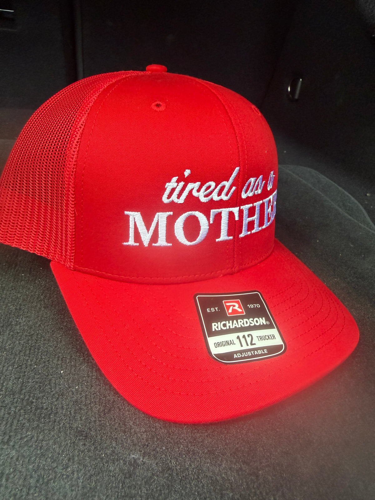 Red snapback cap featuring 'tired as a mother' embroidered on the front.